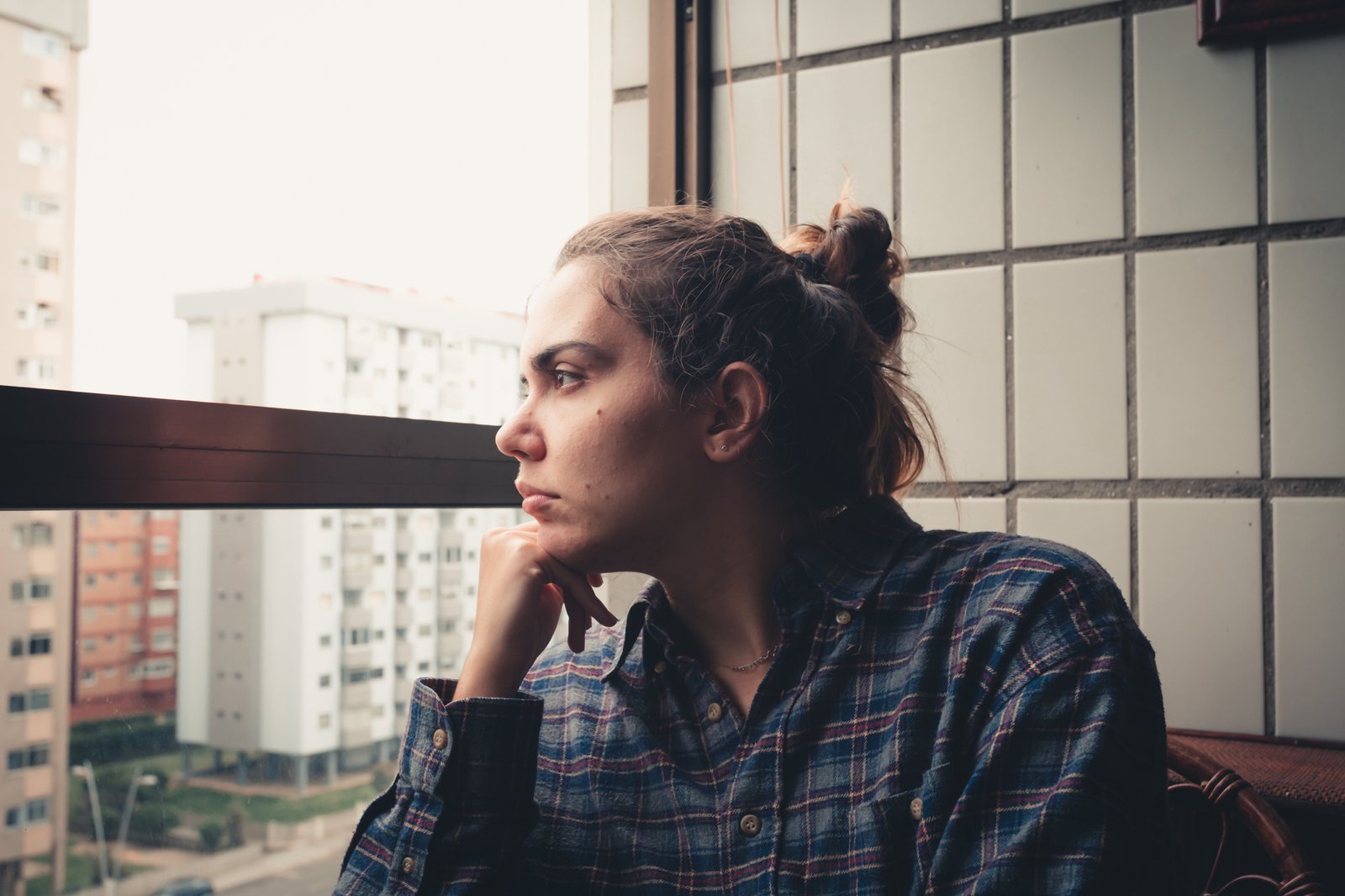 Person schaut nachdenklich aus dem Fenster einer Wohnung